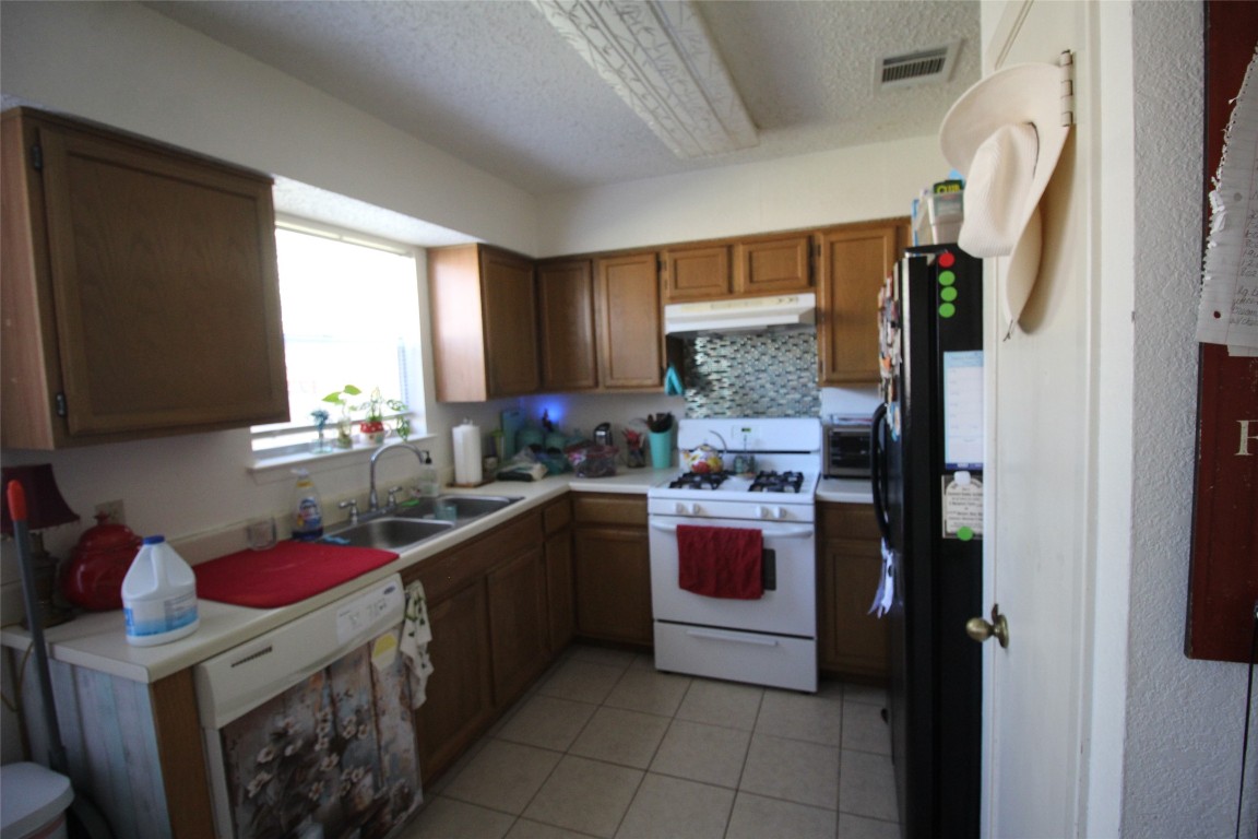 808 Angleton Cove Austin, TX 78748 - Photo 6 of 17 Kitchen with white appliances, brown cabinets, light countertops, a textured ceiling, and under cabinet range hood