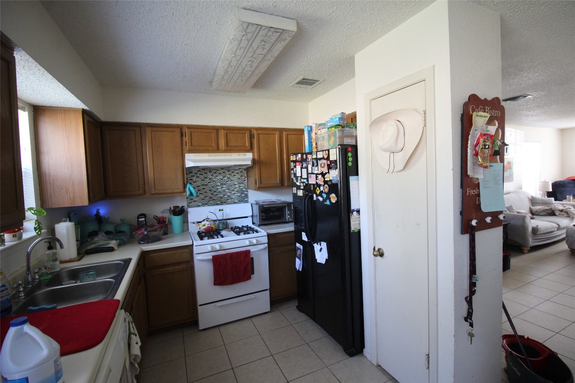 808 Angleton Cove Austin, TX 78748 - Photo 7 of 17 Kitchen with white appliances, light tile patterned floors, a textured ceiling, brown cabinetry, and light countertops