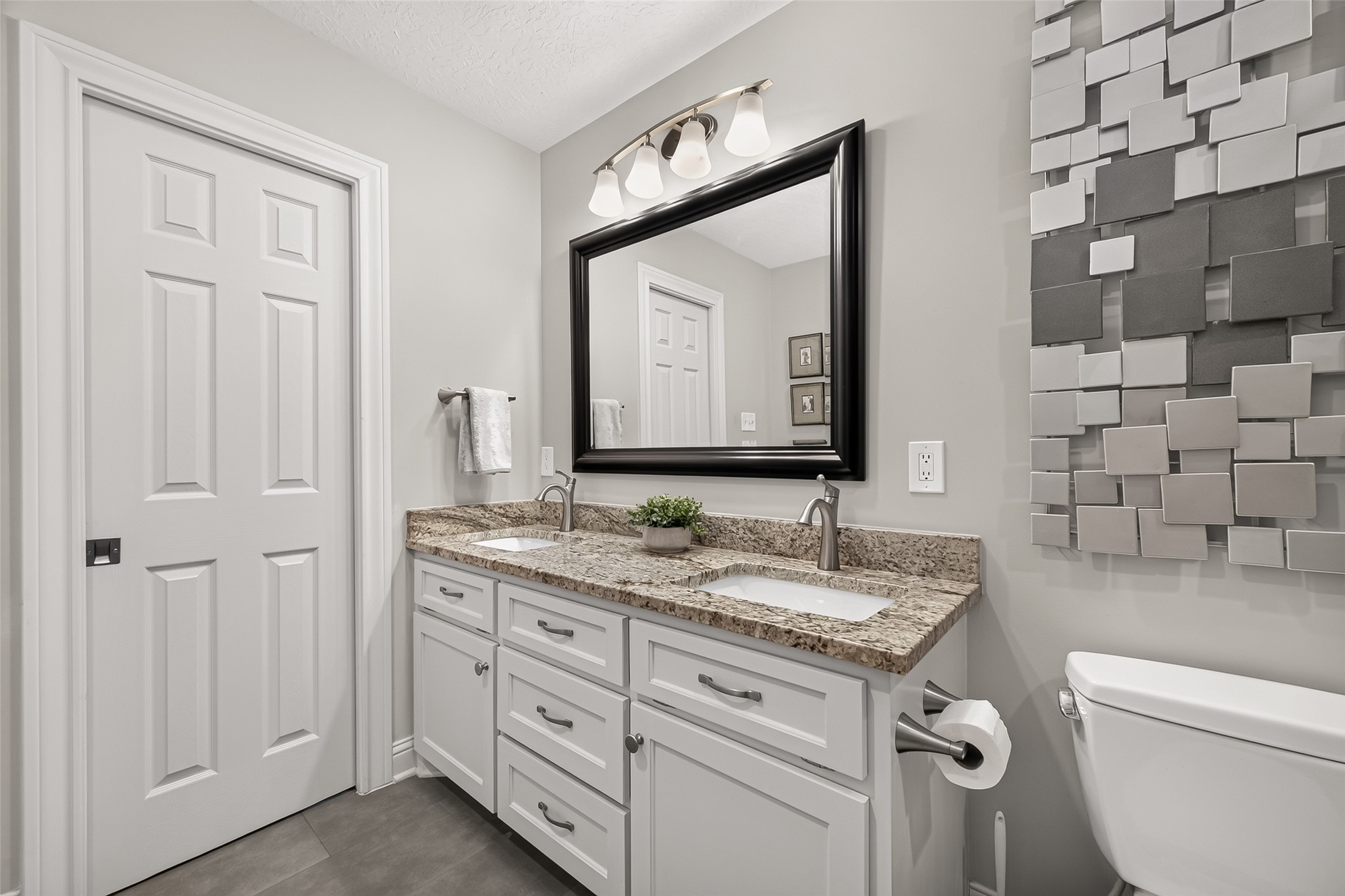 24719 Wilderness Road Spring, TX 77380 - Photo 31 of 42 This bathroom features a modern design with a dual-sink vanity, granite countertops, and sleek fixtures. Neutral tones and stylish wall decor create an inviting atmosphere.