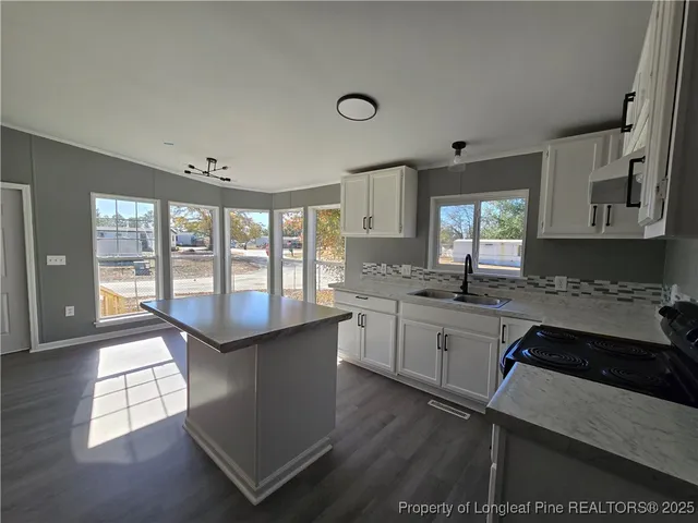 a kitchen with granite countertop a stove a sink and white cabinets with wooden floor