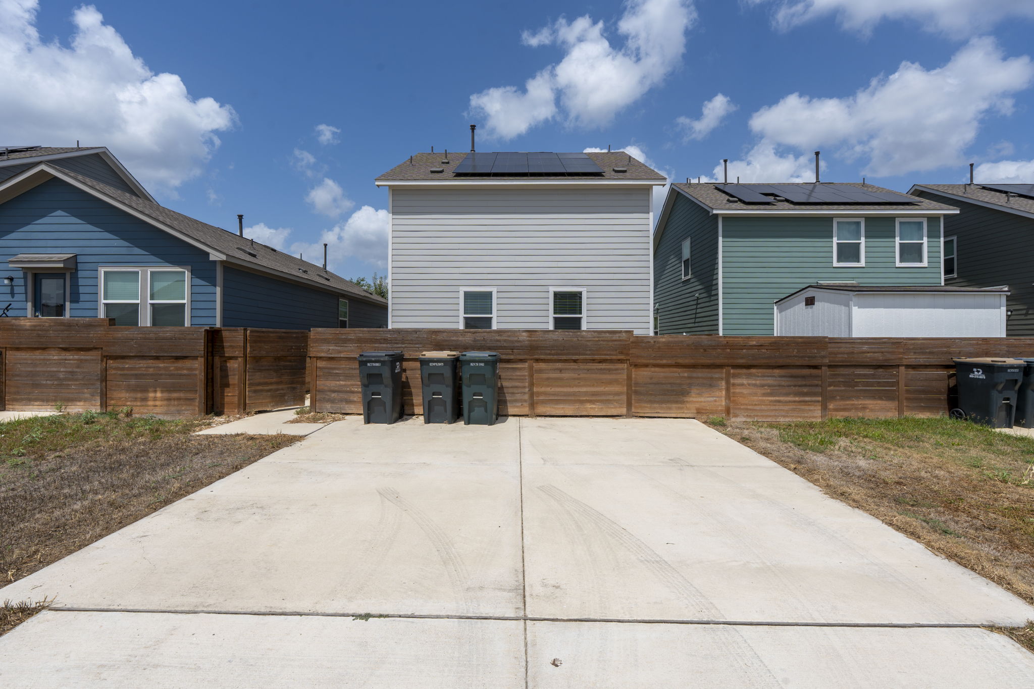 889 Powell Kyle, TX 78640 - Photo 7 of 22 A spacious concrete driveway leads toward a sturdy wooden privacy fence under sunny skies.