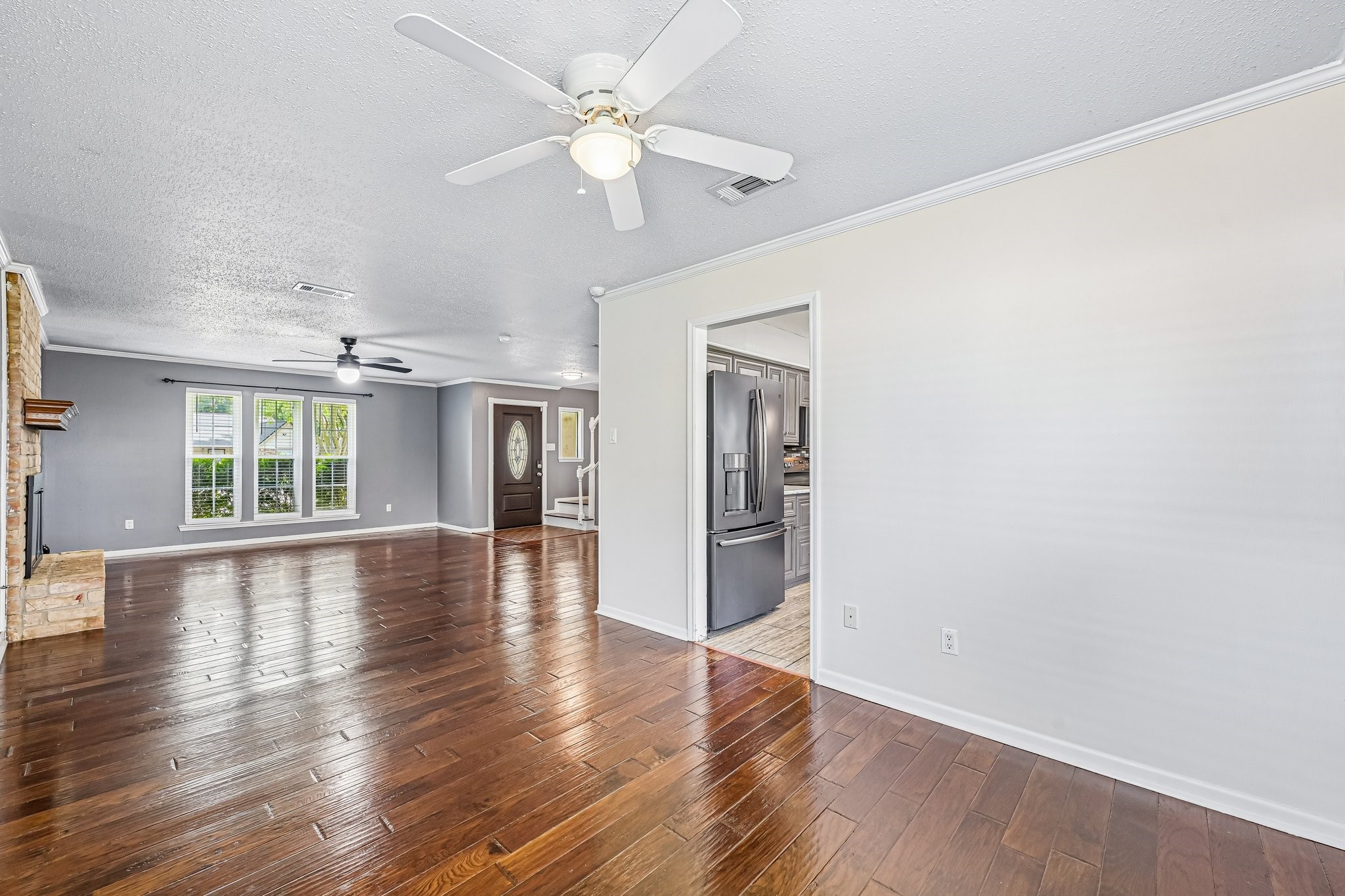 8 Arlington Street Conroe, TX 77301 - Photo 16 of 37 This spacious living area features gleaming hardwood floors, a ceiling fan, and ample natural light from large windows. It seamlessly connects to a modern kitchen with stainless steel appliances.