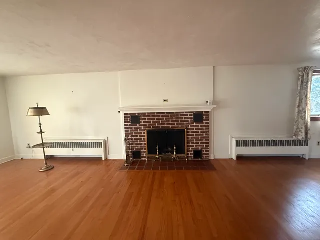 a view of an empty room with wooden floor fireplace and a window