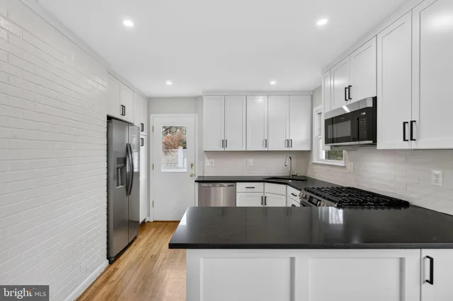 a kitchen with granite countertop a stove a sink a refrigerator and a wooden floor