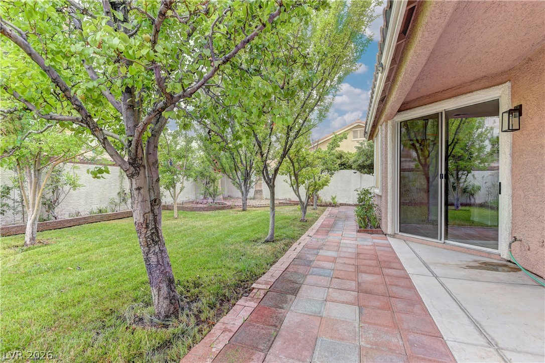 1813 Snow Spring Lane Las Vegas, NV 89134 - Photo 32 of 37 Green landscaping and a paved walkway lead to a sliding glass door for seamless indoor-outdoor living.