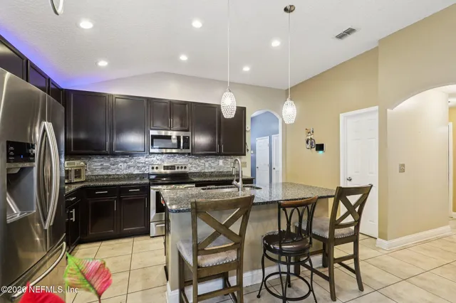 a kitchen with stainless steel appliances kitchen island granite countertop a sink a stove a refrigerator cabinets and chairs