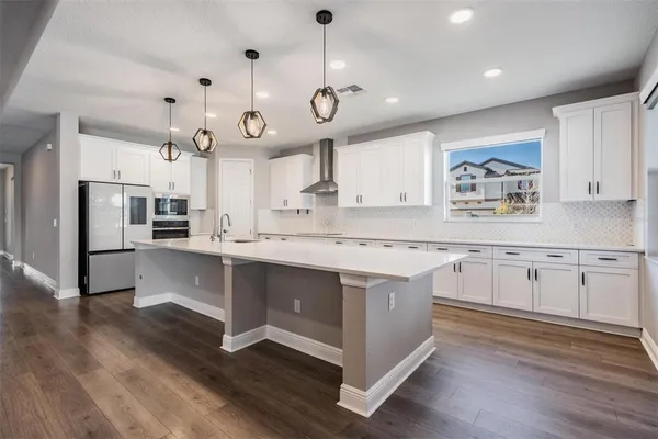 a large kitchen with granite countertop a stove a sink a center island and wooden floor