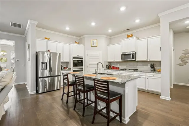 a kitchen with stainless steel appliances a stove a sink a refrigerator white cabinets and wooden floor