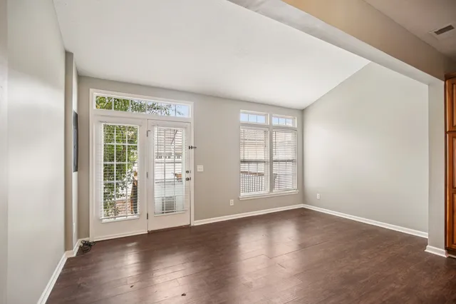 an empty room with wooden floor chandelier fan and windows