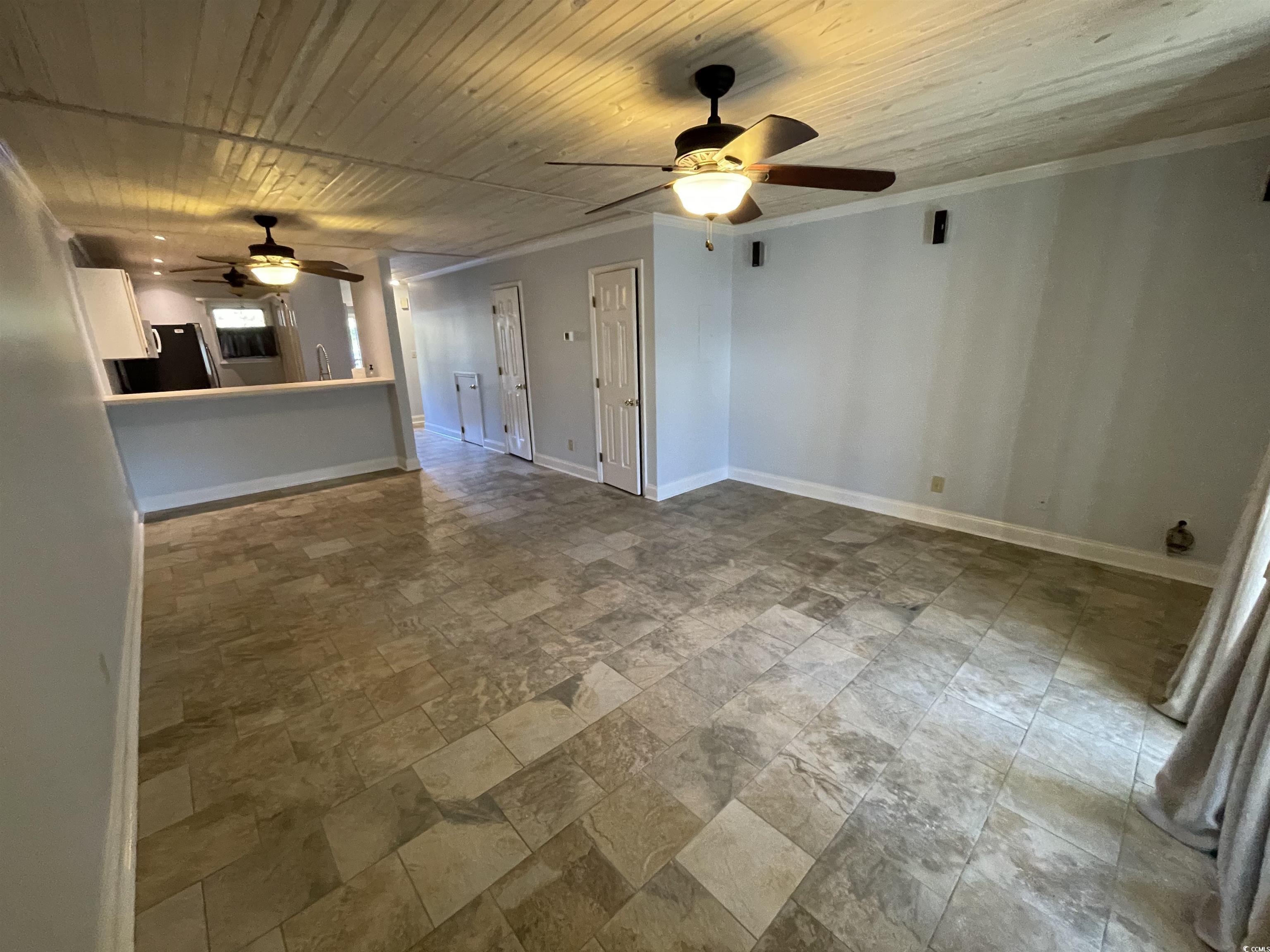 1851 Fairway Ridge Drive, Unit 7E Surfside Beach, SC 29575 - Photo 8 of 29 Unfurnished living room featuring wooden ceiling, stone finish flooring, a ceiling fan, and ornamental molding