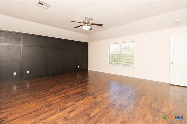 an empty room with wooden floor chandelier fan and windows