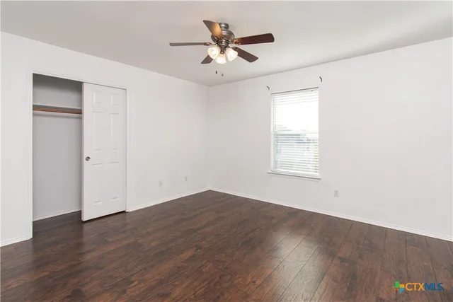 an empty room with wooden floor and a ceiling fan