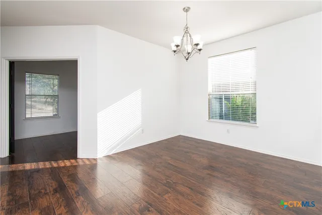 an empty room with wooden floor chandelier and windows