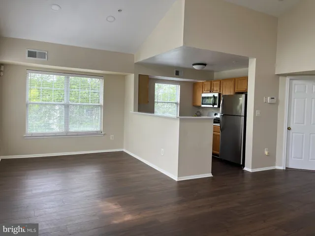 an empty room with wooden floor a kitchen view and windows