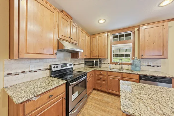 a kitchen with stainless steel appliances granite countertop a refrigerator a sink dishwasher a stove and white countertops with wooden floor