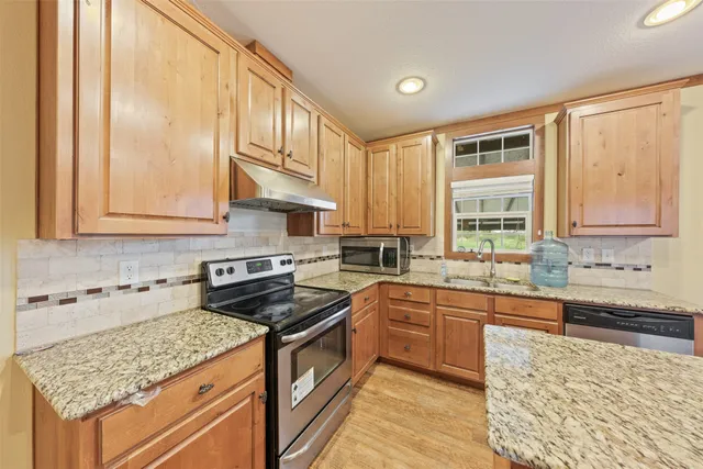 a kitchen with stainless steel appliances granite countertop a refrigerator a sink dishwasher a stove and white countertops with wooden floor