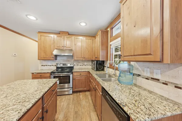 a kitchen with stainless steel appliances granite countertop a refrigerator a oven a sink with wooden cabinets and wooden floor