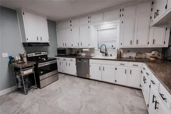 a white kitchen with granite countertop a sink a stove a oven and white cabinets