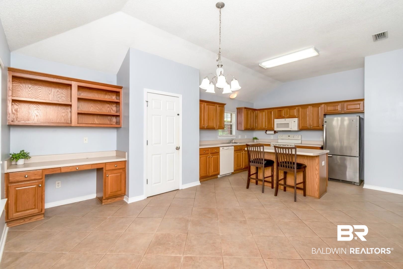 2136 Spring Grove Court Mobile, AL 36695 - Photo 15 of 38 Kitchen area featuring tile flooring, vaulted ceilings, wood cabinetry, a center island with countertop seating, and a built-in desk with shelving