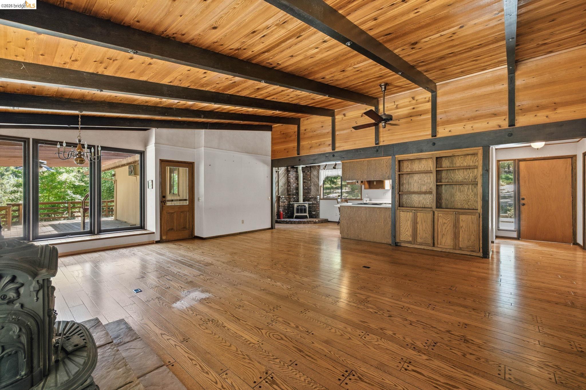 22401 South Fork Road Sonora, CA 95370 - Photo 17 of 34 Spacious open-concept living area featuring a vaulted wood-paneled ceiling with exposed beams, wood-finish flooring, a built-in wood cabinetry unit, a ceiling fan, and large windows with a glass door opening to an outdoor deck