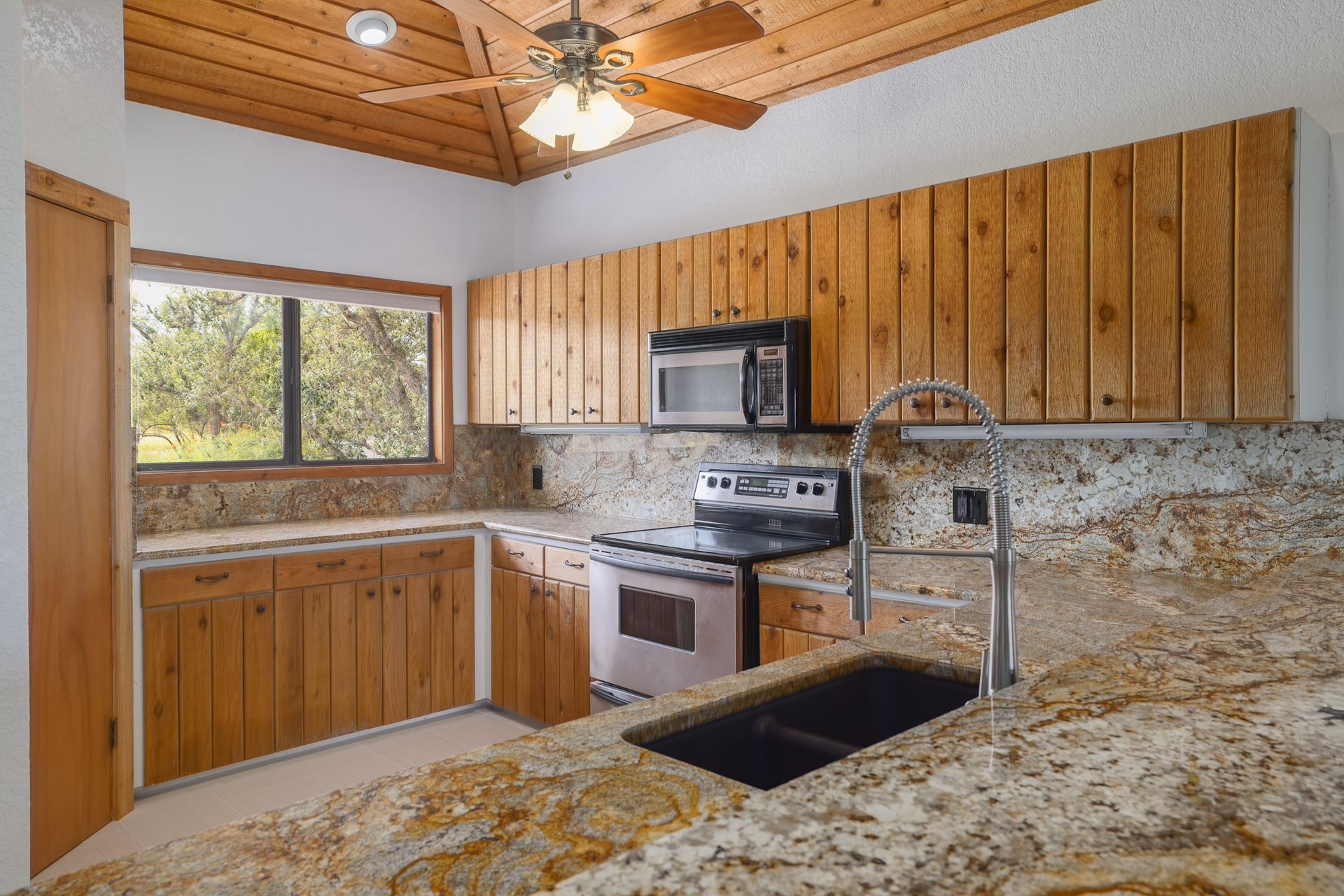 313 Kendall Road Spicewood, TX 78669 - Photo 8 of 34 Kitchen featuring electric stove, tasteful backsplash, brown cabinetry, black microwave, and light stone countertops