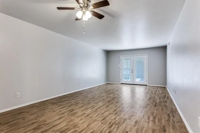 a view of an empty room with wooden floor and a chandelier fan