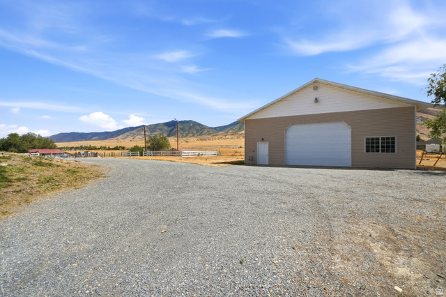 4468 North Droubay Road Tooele, UT 84074 - Photo 39 of 60 Gravel driveway leading to a large building featuring a roll-up garage door, multiple windows, and a pedestrian entry door