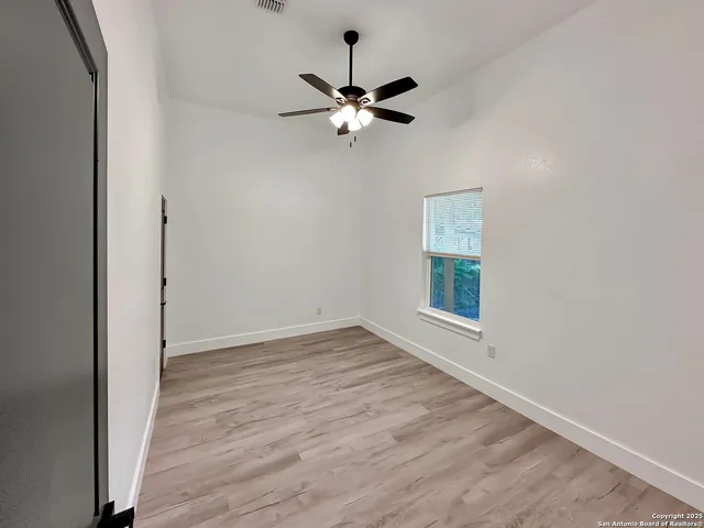 an empty room with wooden floor fan and windows