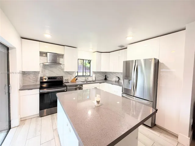 a large kitchen with stainless steel appliances granite countertop a sink a stove and a refrigerator