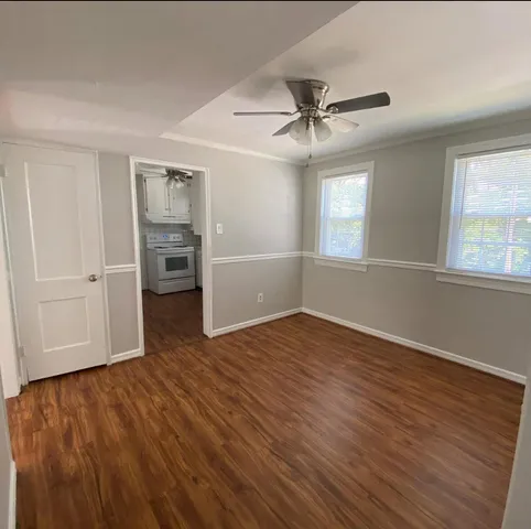 an empty room with wooden floor chandelier fan and windows