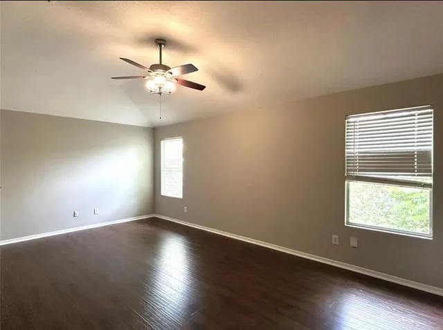 an empty room with wooden floor fan and windows