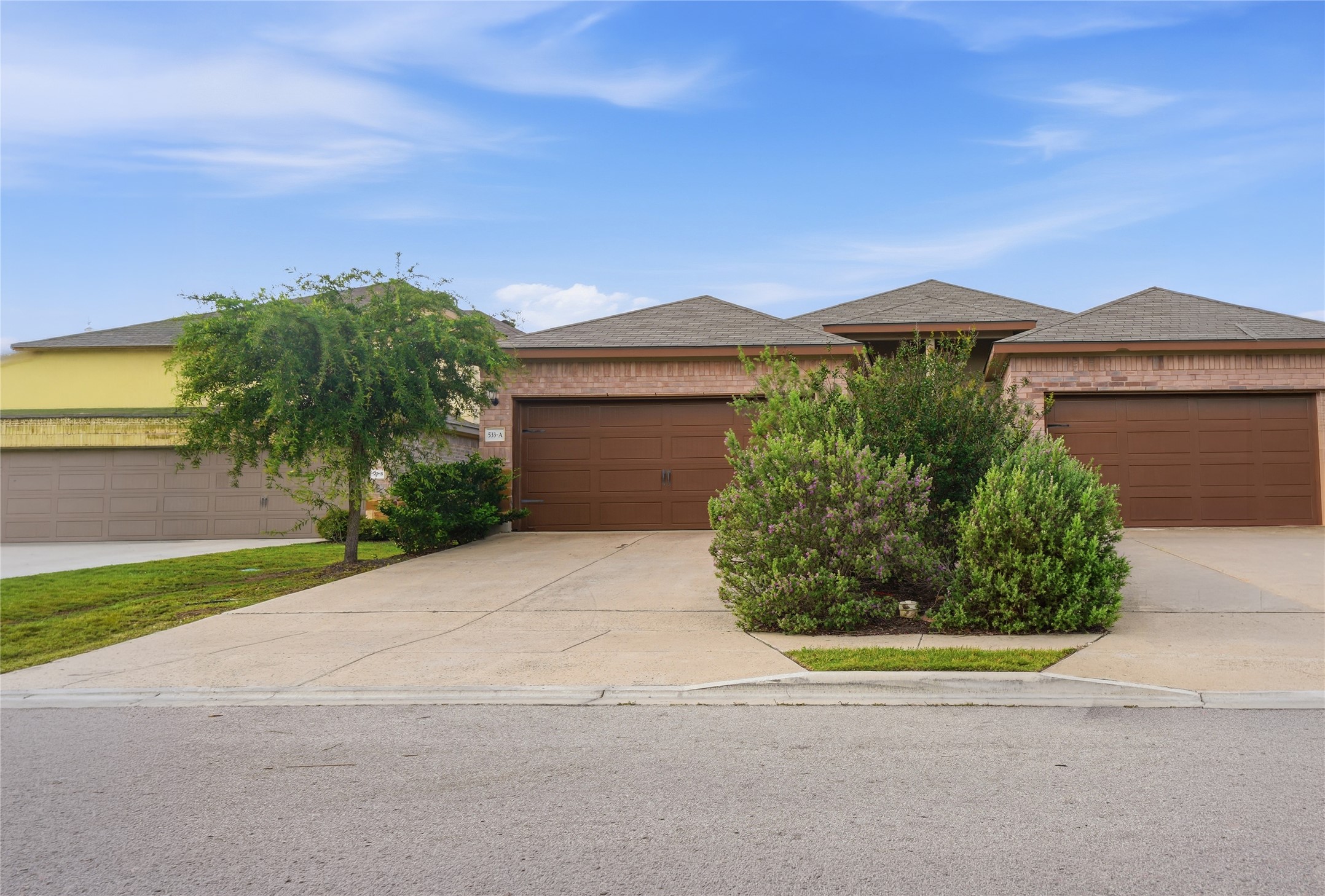 533 Jack Rabbit Lane, Unit A Buda, TX 78610 - Photo 4 of 34 A well-maintained brick facade home awaits, featuring an attached garage and mature landscaping.