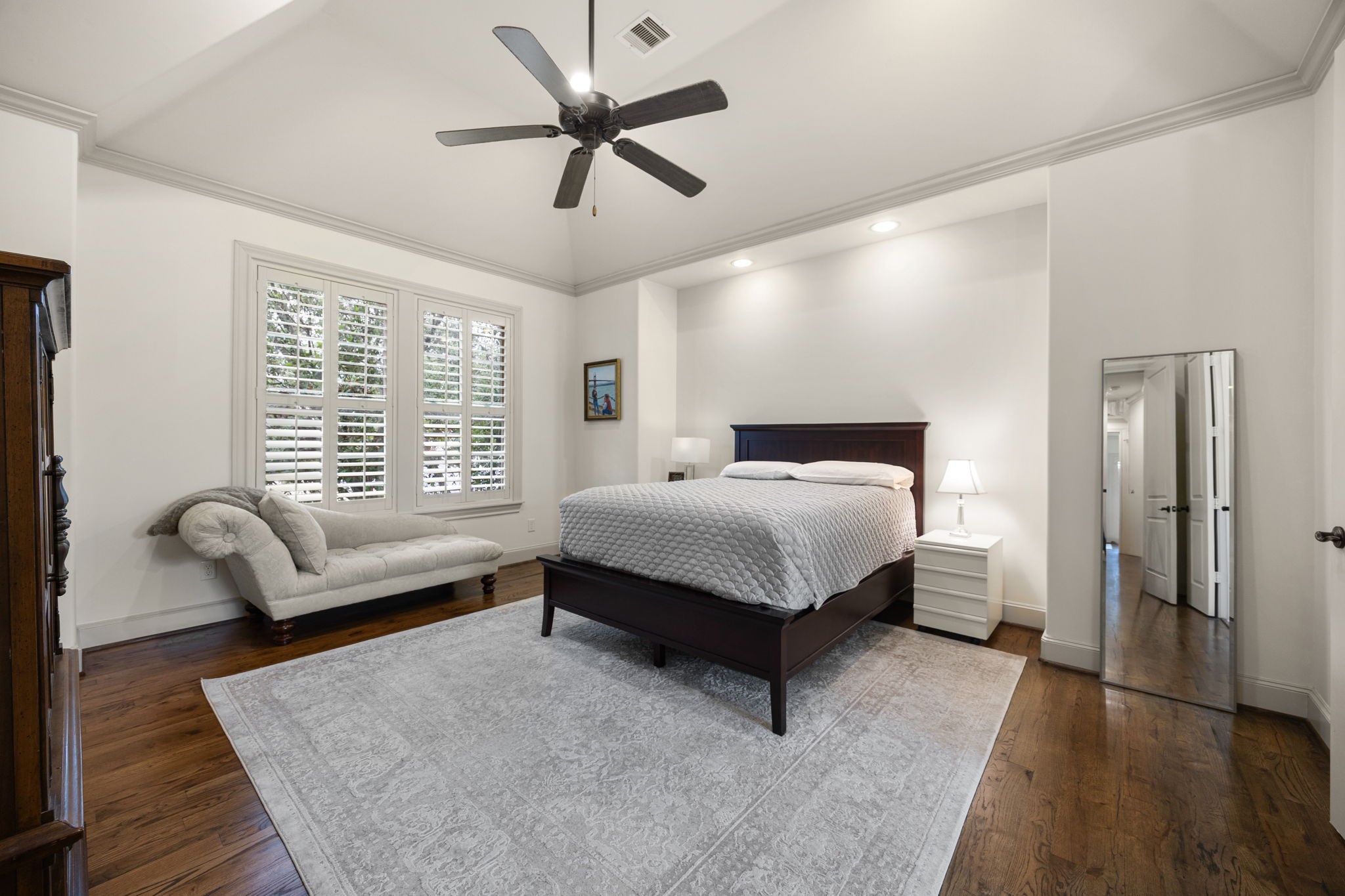 310 West Bell Street Houston, TX 77019 - Photo 31 of 44 This spacious primary bedroom features elevated finishes such as a vaulted ceiling, crown moulding, hardwood floors, and shuttered windows. The neutral tones create an elegant place to retreat.