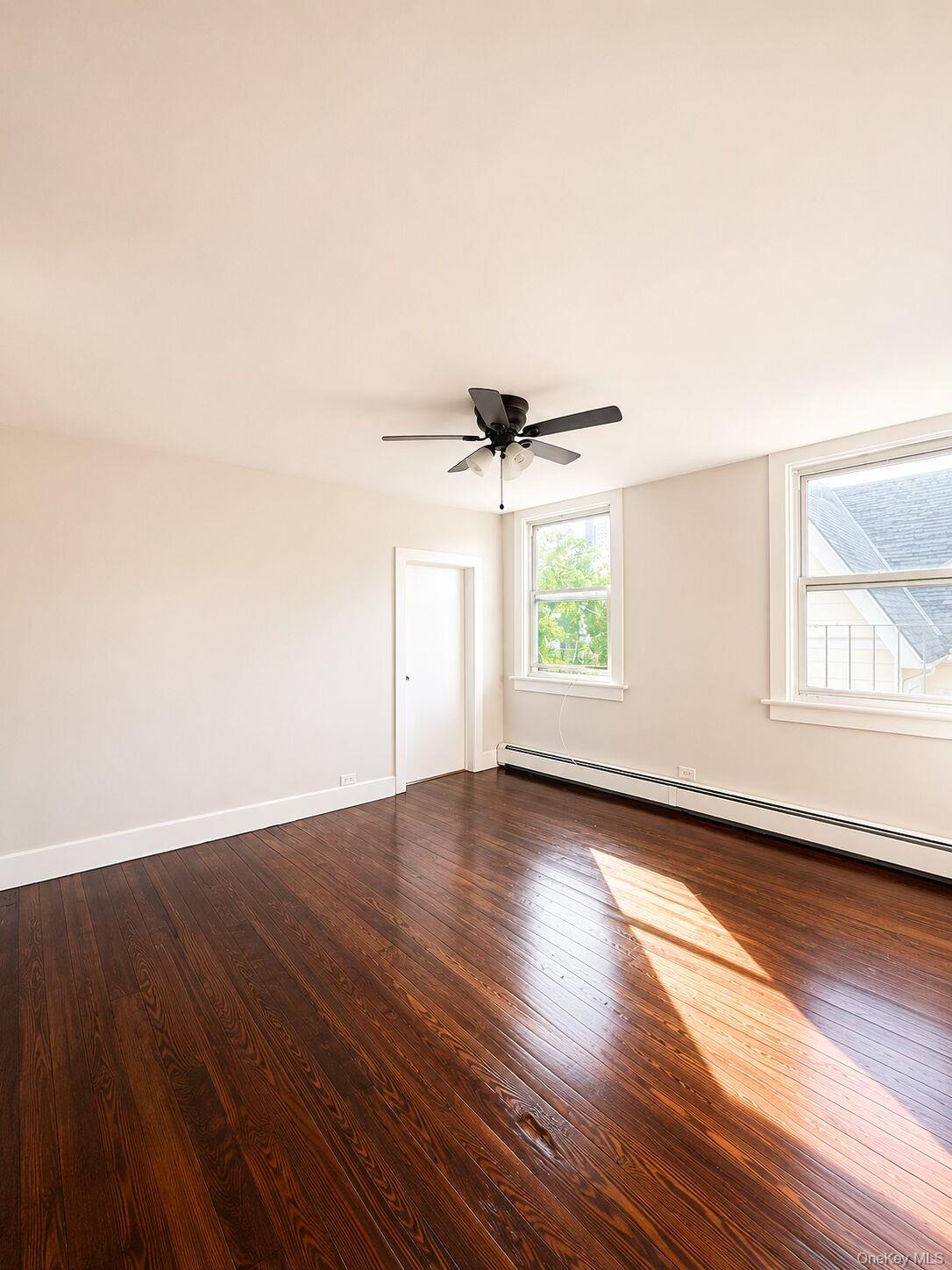 79 Division Street, Unit 3 New Rochelle, NY 10805 - Photo 10 of 17 Spacious living room featuring dark wood-finish flooring, white baseboards, and light neutral walls.