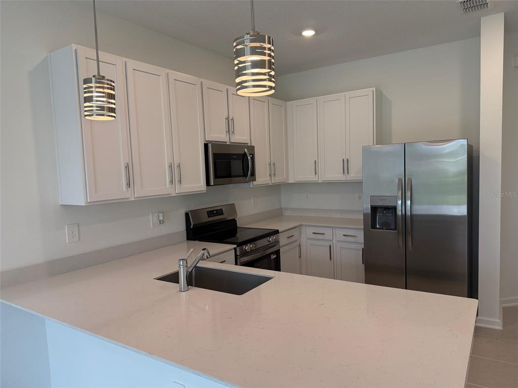 2691 Skyline Loop Kissimmee, FL 34758 - Photo 16 of 27 a kitchen with a refrigerator a microwave a stove and white cabinets