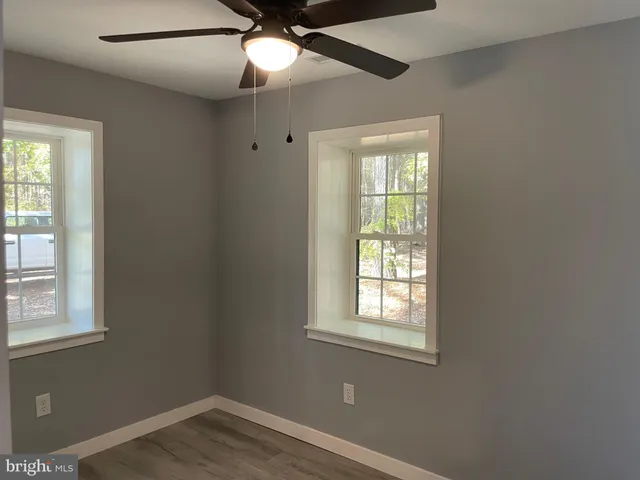 an empty room with wooden floor fan and windows