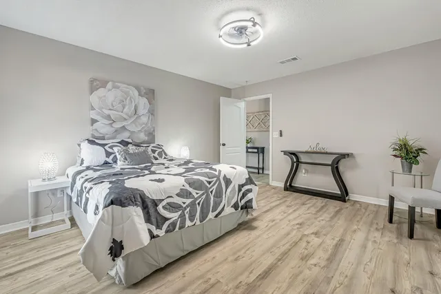a bedroom with a bed and a lamp on table with wooden floor