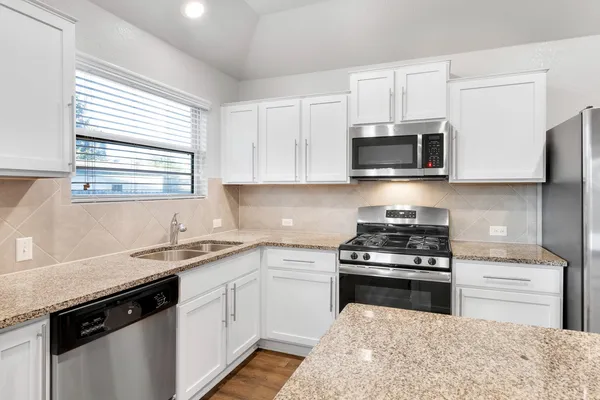 a kitchen with granite countertop white cabinets appliances and a window