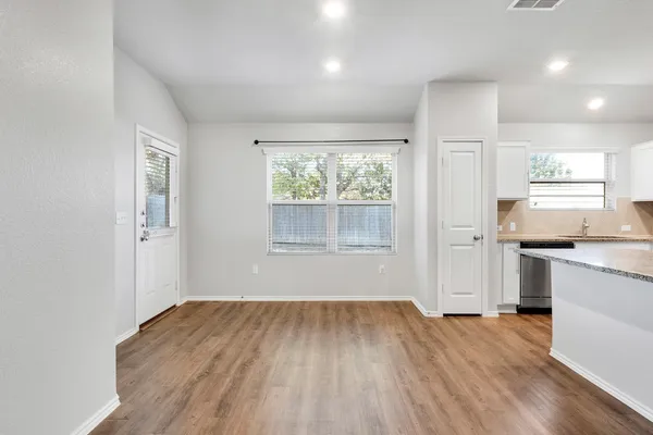 a view of a kitchen and an empty room with wooden floor and a window