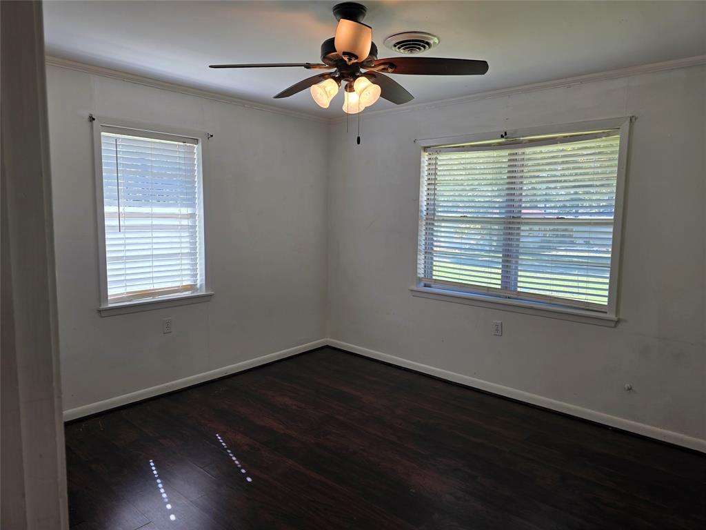 103 North Magnolia Street Plain Dealing, LA 71064 - Photo 17 of 26 Empty room featuring dark wood-style floors, crown molding, and a ceiling fan