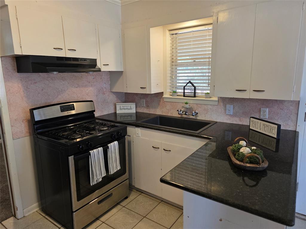 103 North Magnolia Street Plain Dealing, LA 71064 - Photo 8 of 26 Kitchen featuring stainless steel gas stove, tasteful backsplash, light tile patterned flooring, under cabinet range hood, and dark stone countertops