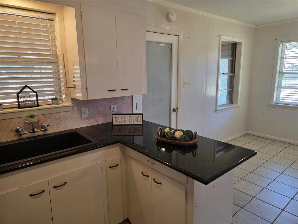 103 North Magnolia Street Plain Dealing, LA 71064 - Photo 9 of 26 Kitchen featuring a peninsula, light tile patterned floors, dark stone counters, tasteful backsplash, and ornamental molding