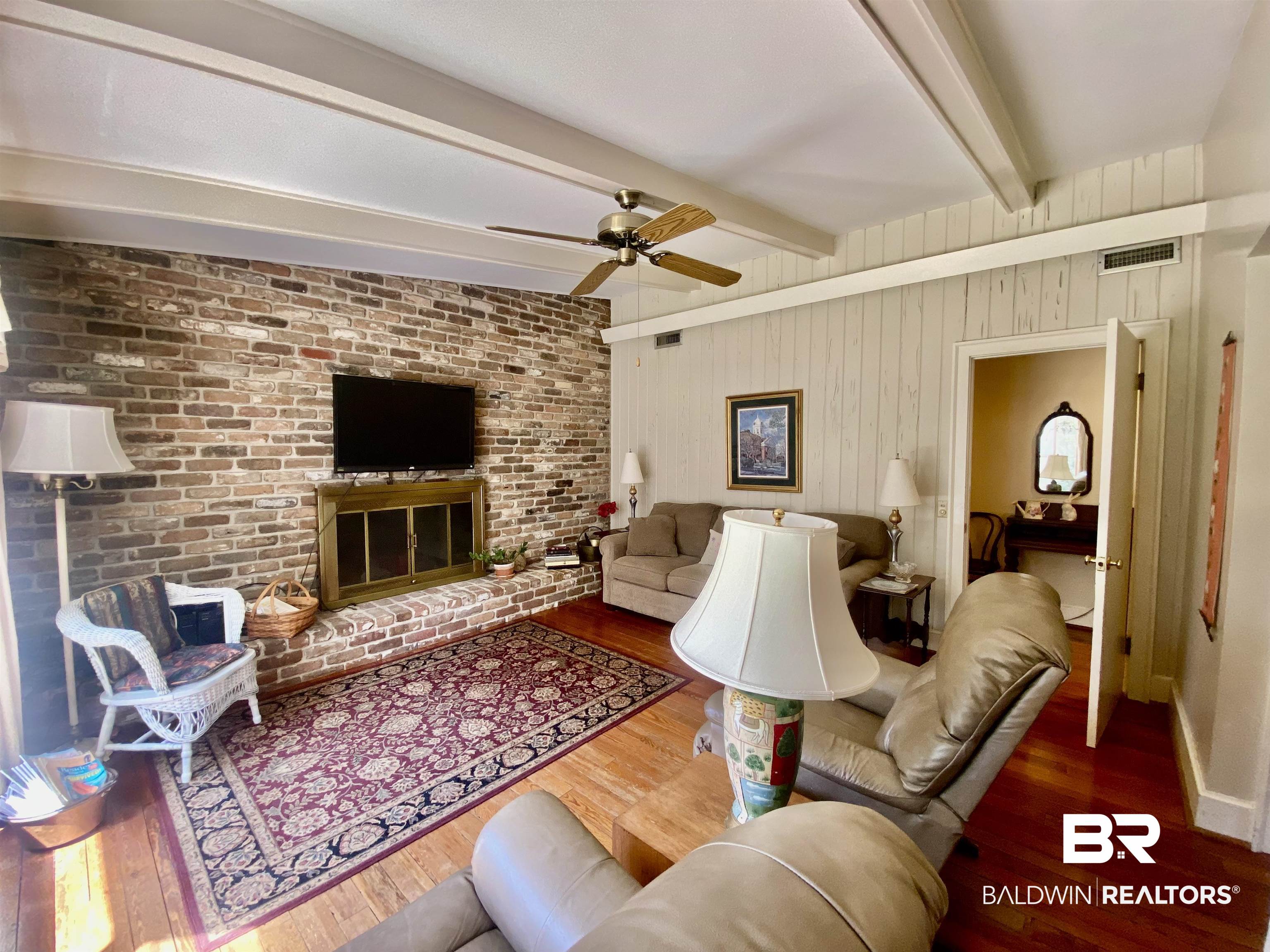 272 Longleaf Circle Monroeville, AL 36460 - Photo 12 of 38 Den with beamed ceiling, a brick fireplace, wooden walls, hardwood / wood-style floors, and ceiling fan.