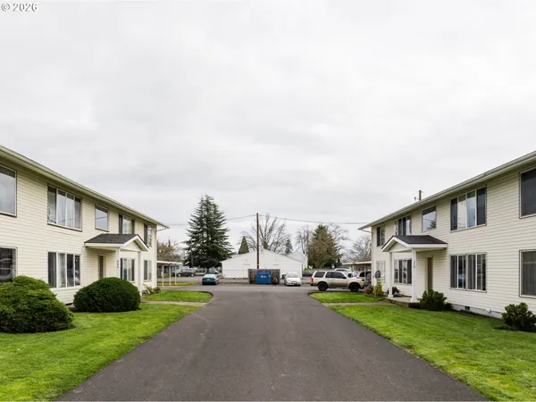 a view of a white house next to a yard with big trees