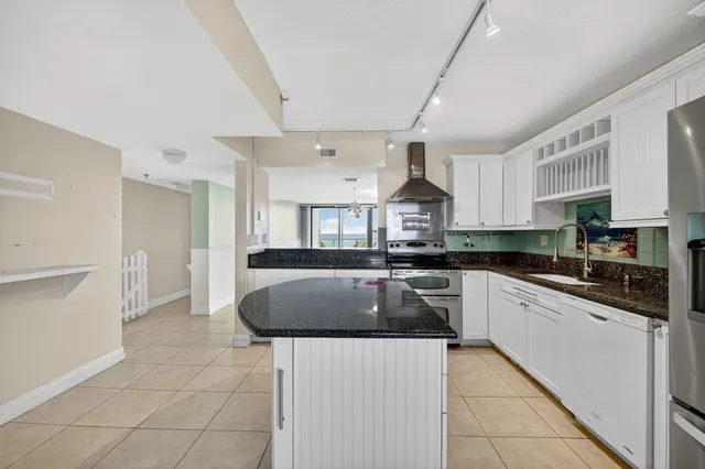 a kitchen with stainless steel appliances granite countertop a sink a stove a refrigerator a microwave oven and white cabinets