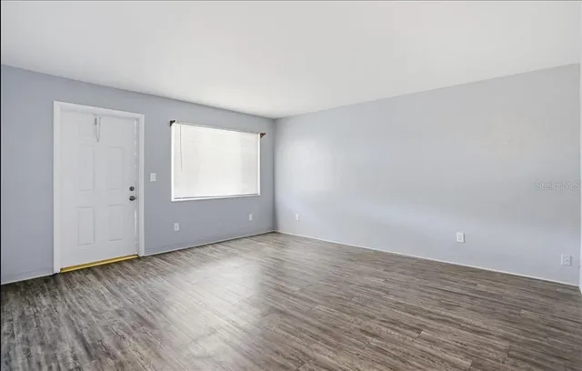 a view of an empty room with wooden floor and a window