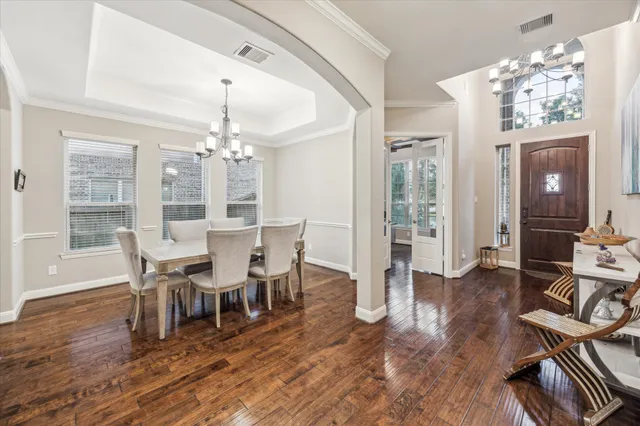 a dining room with wooden floor a chandelier a glass table and chairs