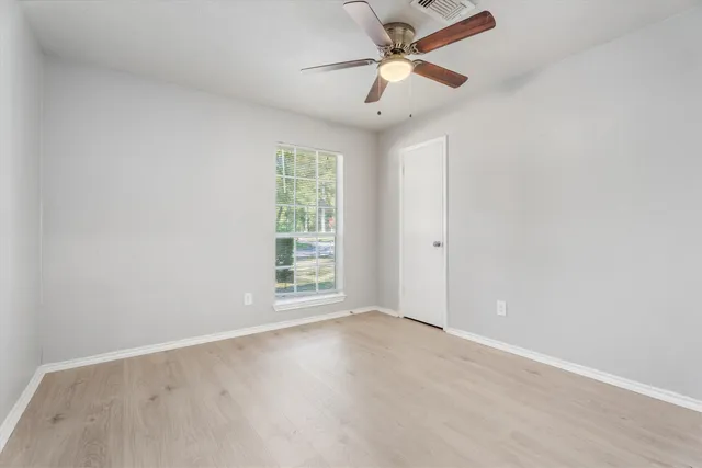 an empty room with wooden floor fan and windows