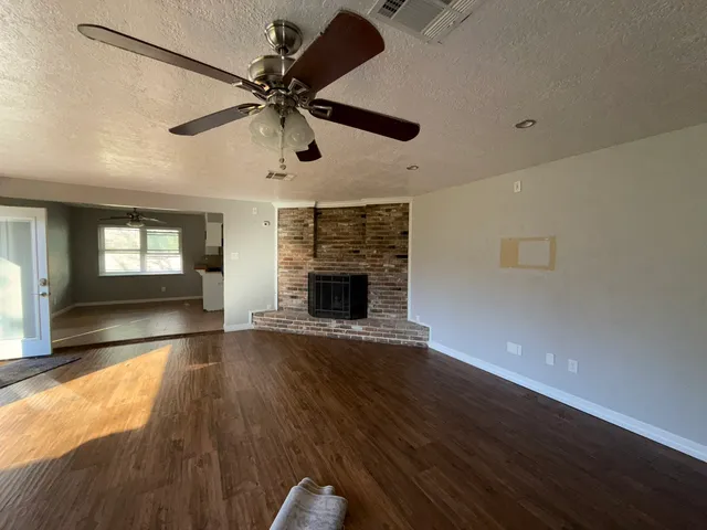 a view of an empty room with wooden floor fireplace and a window
