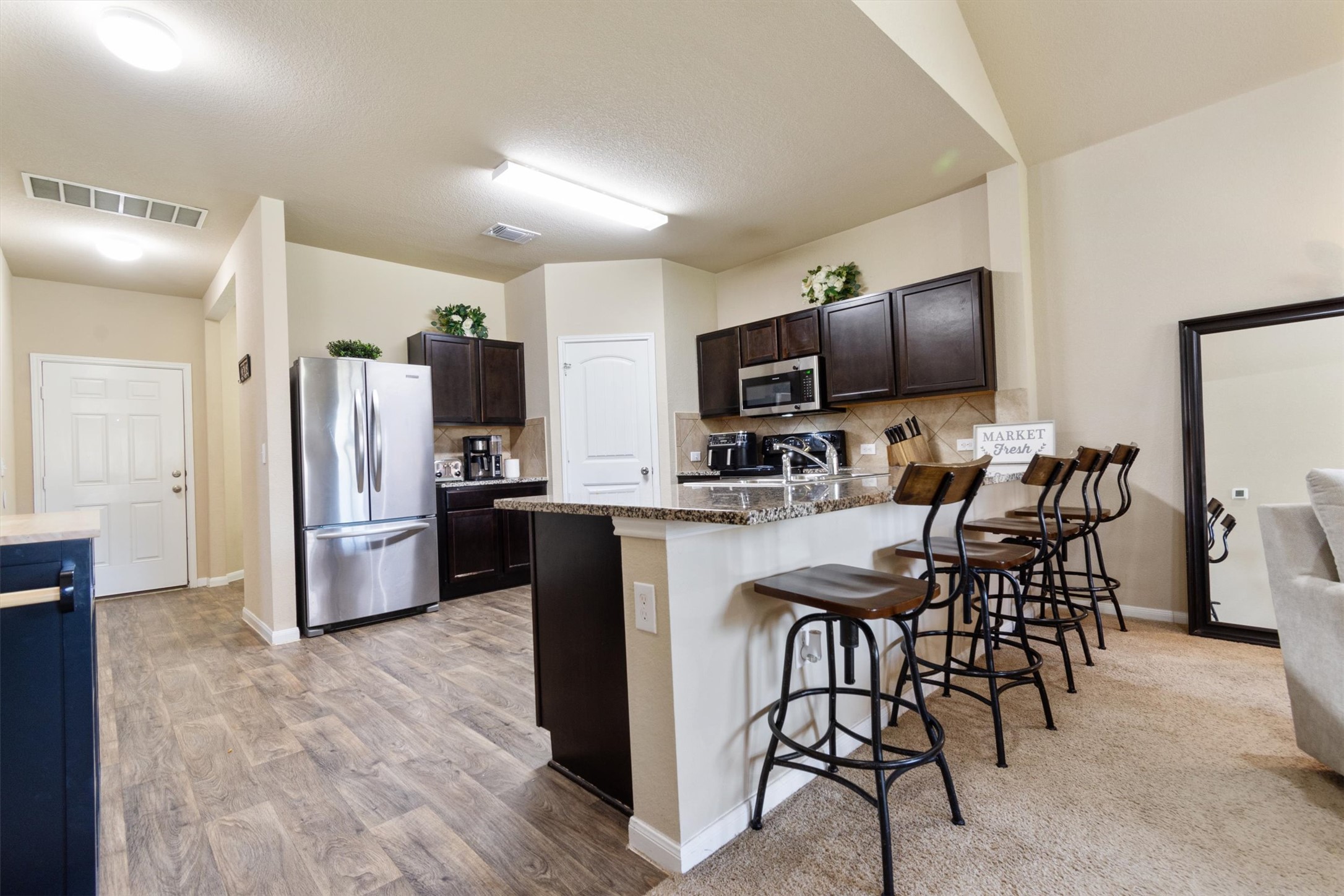 11620 Carbrook Road Manor, TX 78653 - Photo 5 of 40 a kitchen with refrigerator a microwave a stove and island with wooden floor